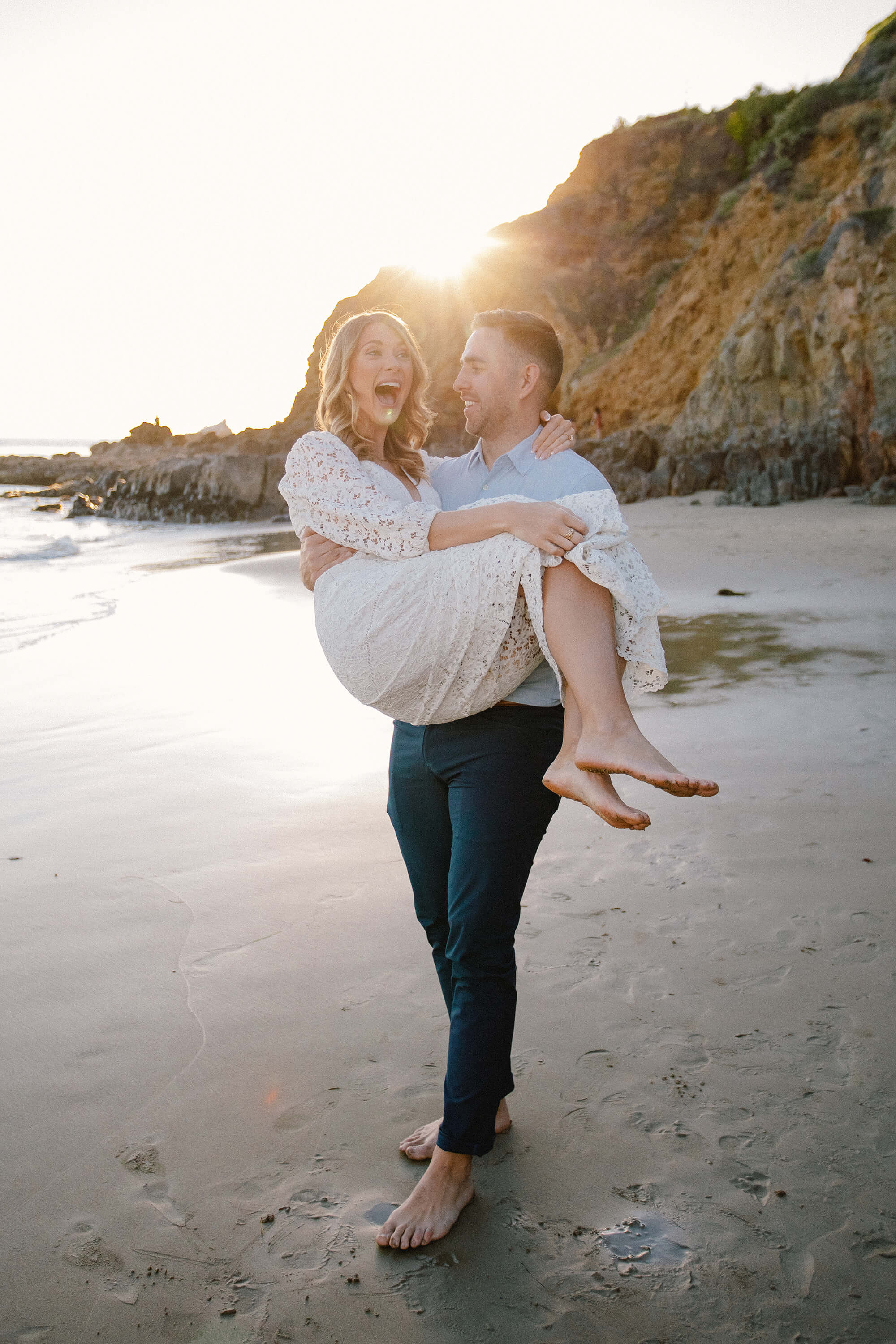 JJ carrying Kait on the beach with the sunset behind them.
